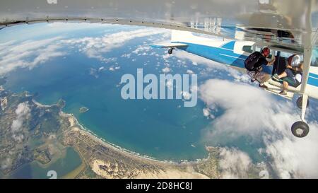 Fallschirmspringer hängen aus dem Flugzeug, in einem paradiesischen Ort. Stockfoto