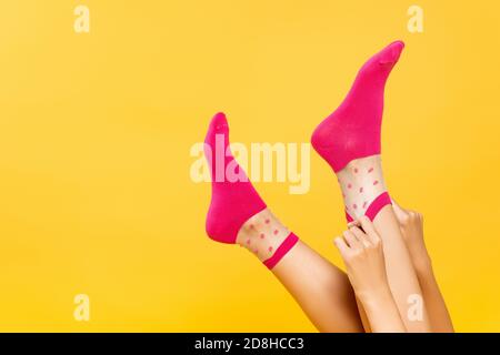 Beschnittene Ansicht der Frau setzen rosa Socken auf Beine isoliert Auf gelb Stockfoto