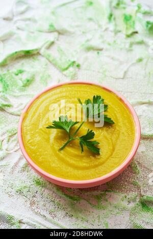 Eine Keramikschale mit Blumenkohlpüree, gekrönt mit einem Zweig Petersilie und mit Olivenöl gekleidet, auf einer strukturierten Oberfläche platziert Stockfoto