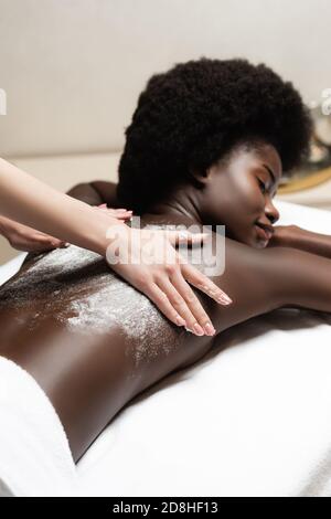 Masseur massiert afroamerikanische Frau mit Peeling im Spa-Salon Stockfoto