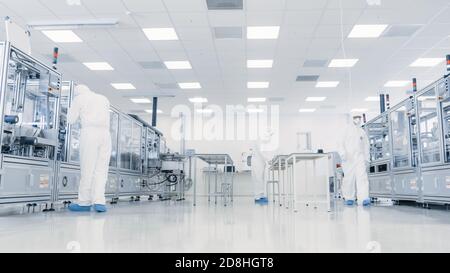 Team von Wissenschaftlern in sterilen Anzügen, die mit Computern, Mikroskopen und modernen Industriemaschinen im Labor arbeiten. Produkt Stockfoto