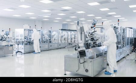 Sterile High Precision Manufacturing Laboratory wo Wissenschaftler in Protective Overall drehen sich auf Maschinen, verwenden Computer und Mikroskope, tun Stockfoto