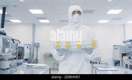 Wissenschaftler im Schutzanzug trägt Koffer mit Fertigprodukt durch Labor. Anlage mit modernen Industriemaschinen. Produktherstellung Stockfoto