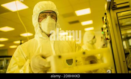 Wissenschaftler in steriler Schutzkleidung arbeiten an einer modernen industriellen 3D-Druckmaschine. Pharmazie, Biotechnologie und Halbleiter Stockfoto