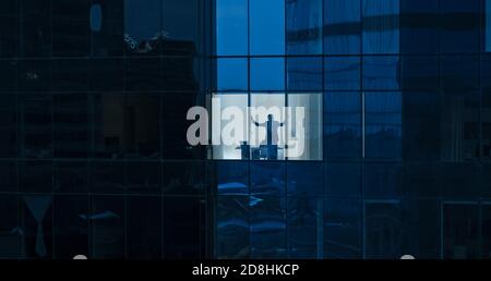 Luftaufnahme: Von draußen ins Bürogebäude mit Geschäftsmann, der aus dem Fenster schaut. Aufnahme der Wolkenkratzer des Finanzgeschäftsviertels in der Stockfoto