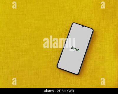 LOD, Israel - 8. Juli 2020: Fiverr App Launch Screen mit Logo auf dem Display eines schwarzen Smartphone auf einem gelben Stoff Hintergrund. Draufsicht FLA Stockfoto