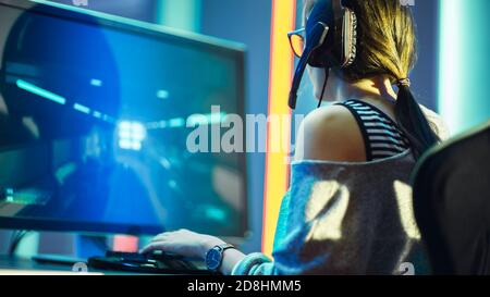 Aufnahme der schönen Pro Gamer Girl spielt in FPS Video Game auf ihrem Personal Computer, Casual Cute Geek trägt Brille und Headset. Neon-Zimmer Stockfoto