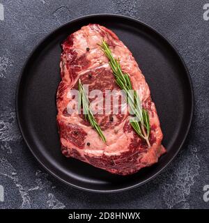 Frisches rohes Rindersteak auf schwarzem Teller, Draufsicht. Stockfoto