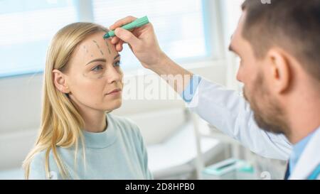 Over the Shoulder Shot eines plastischen Kosmetikchirurgen zeichnet Linien auf ein Gesicht eines schönen weiblichen Modells für die Facelift-Operation. Stockfoto