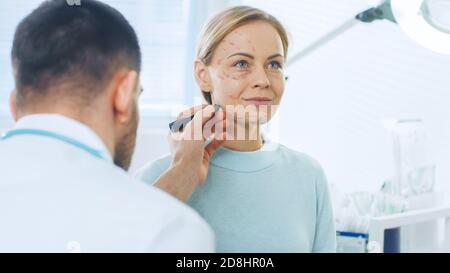 Over the Shoulder Shot eines plastischen Kosmetikchirurgen zeichnet Linien auf ein Gesicht eines schönen weiblichen Modells für die Facelift-Operation. Stockfoto