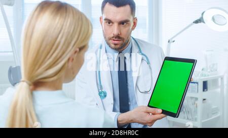 Über die Schulter Aufnahme einer Patientin im Gespräch mit einem professionellen Arzt, der ihren digitalen Tablet-Computer mit Mock-up Green Screen zeigt. Stockfoto