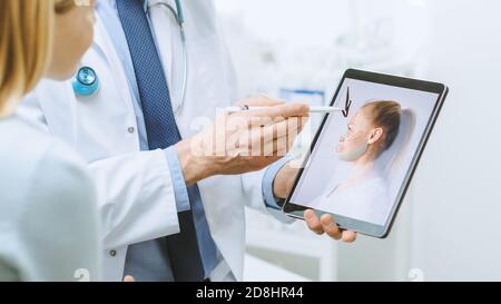Plastischer kosmetischer Chirurg konsultiert Frau über Gesichtslift-Chirurgie, Er zeigt auf Digital Tablet Computer-Bildschirm, die Arten von Facelift, Stirn Stockfoto