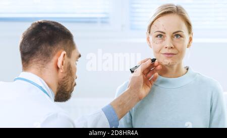 Over the Shoulder Shot eines plastischen Kosmetikchirurgen zeichnet Linien auf ein Gesicht eines schönen weiblichen Modells für die Facelift-Operation. Stockfoto