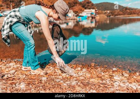 Der Schutz der Umwelt und Earth Day. Eine Freiwillige nimmt eine Plastikflasche am Ufer eines Sees oder Flusses. Stockfoto