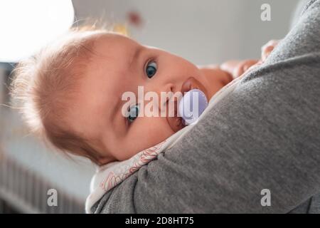 Eine Mutter lullt ein Baby in ihren Armen mit einem Schnuller im Mund. Nahaufnahme Porträt eines Kindes. Konzept der Mutterschaft. Stockfoto