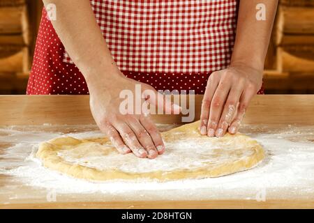 Weibliche Hände, die Teig zum Backen auf hölzernem Backbrett auf der Küchentheke vorbereiten. Küchentisch mit leerem Platz für Lebensmittel und Produkte. Stockfoto