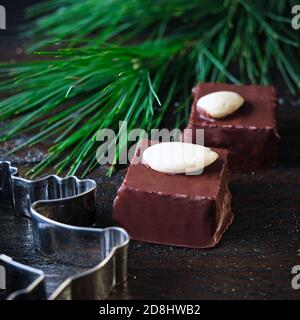 Marzipankuben mit Schokoladenvereisung auf einem schwarzen Kühlgitter, verziert mit Kiefernzweig, Zimtstangen und Anissternen, Tannenzapfen Stockfoto