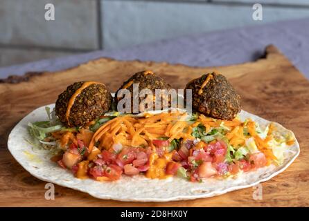 Gebratene Falafalbällchen mit buntem Salat in einem Wrap, mit Sauce darüber. Stockfoto