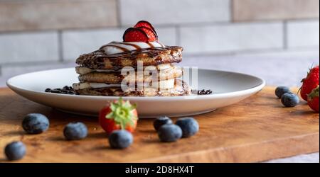 Veganer Blaubeerpfannkuchen-Stapel, hergestellt mit proteinreichem Kamut-Mehl und Leinsamen, mit Kokosrahm-Belag und gekrönt mit einer Erdbeere. Stockfoto