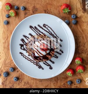 Veganer Blaubeerpfannkuchen-Stapel, hergestellt mit proteinreichem Kamut-Mehl und Leinsamen, mit Kokosrahm-Belag und gekrönt mit einer Erdbeere. Stockfoto