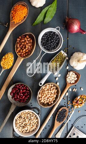 Hülsenfrüchte pulsieren auf blauem Tischhintergrund. Kugeln, Schüsseln und Schöpflöffel mit trockener vegetarisch gesunder Nahrung. Draufsicht, flach liegend Stockfoto