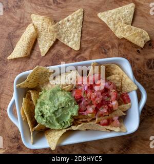 Nachos mit Avocado Guacamole und Salsa, serviert in einer weißen Schüssel auf einer Holzplatte. Stockfoto