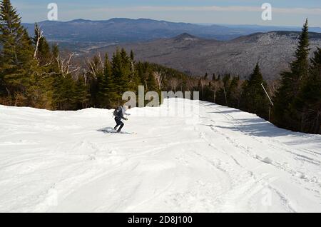 Skifahrer steigt Stowe Mountain Resort (Mt. Mansfield), Stowe, Vermont, USA, im Frühjahr nach dem Skifahren den Berg hinauf. Stockfoto