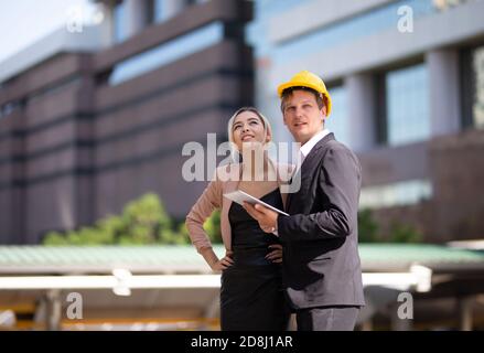 Ingenieurin mit weißem Helm auf einer Baustelle mit Geschäftsmann im Gespräch über Arbeitsplan, Ingenieur und archite Stockfoto