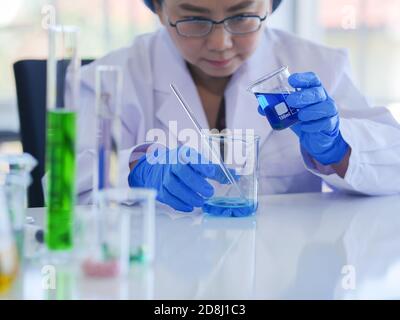 Leitende Wissenschaftlerinnen sind dabei, 2 Arten von Flüssigkeit in einem Becher für ein wissenschaftliches Experiment zu mischen, um Biochemie oder anderweitig zu entwickeln. Weibliche Wissenschaftler Stockfoto