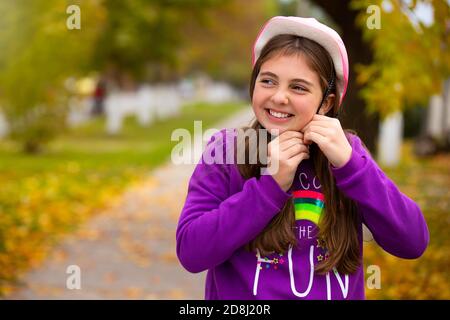 Mädchen in einem trendigen rosa Helm mit einem glücklichen Lächeln in einem Herbstpark. Urlaubskonzept und Zeit verbringen Stockfoto