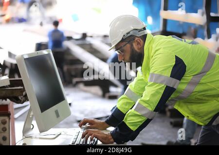 Bauarbeiter mit Laptop, Techniker mit Selbstvertrauen gegen Maschinenumgebung im Werk Stockfoto