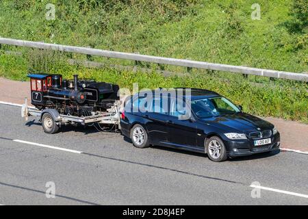 2010 schwarz BMW 318d Es 1995cc Diesel Nachlass Schleppen Miniatur-Modell Eisenbahn Dampfzug auf Anhänger; Fahrzeugverkehr, Fahrzeuge bewegen, Autos, Fahrzeug fahren auf britischen Straßen, Motoren, Fahren auf der Autobahn M61 Autobahn UK Straßennetz. Stockfoto