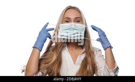 Junge Krankenschwester in Robe und Handschuhen legt eine Maske auf ihr Gesicht. Stockfoto