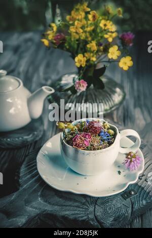 Heilkräutertee mit Kamillenblüten und einem Bouquet von Wildblumen in einer schönen Tasse auf einem rustikalen Holzhintergrund. Rustikales Stillleben Stockfoto