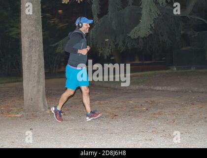 Mailand, Italien, 5. Oktober 2018: Ein sportlicher Mann mit Kopfhörern hört Musik und joggt in einem dunklen Herbstpark spät in der Nacht Stockfoto