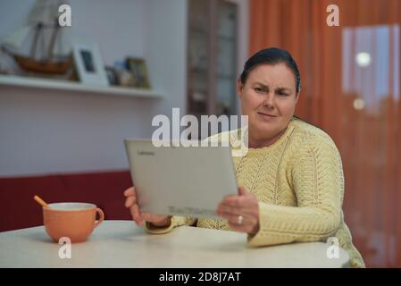Ältere Frau in gelben Pullover suchen Laptop mit unglücklichen Gesicht Stockfoto