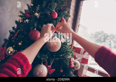 Beschnitten Foto von jungen Mädchen Hände hängen Kugeln Glocken Spielzeug golden Ball immergrünen Baum tragen roten Pullover dekoriert Wohnzimmer In Innenräumen Stockfoto