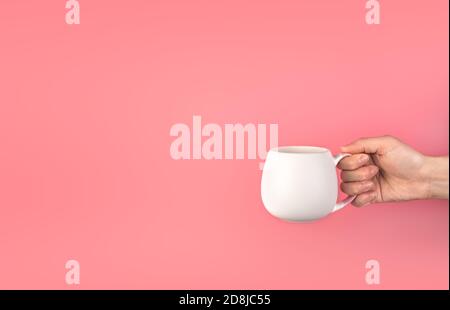 Die Hand einer Frau hält einen weißen Becher auf einem rosa Hintergrund. Stockfoto