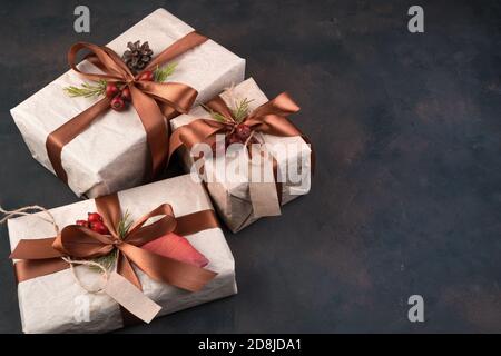 Drei Geschenke in beige Geschenkpapier gebunden mit braunen Bändern auf braun. Stockfoto