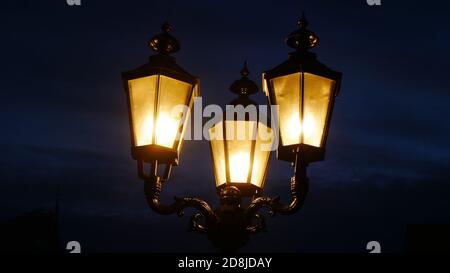 Nahaufnahme von drei altmodischen Laternen in der Nacht mit hell Gelbes Licht und ein unheimlicher dunkler Himmel im Hintergrund Stockfoto