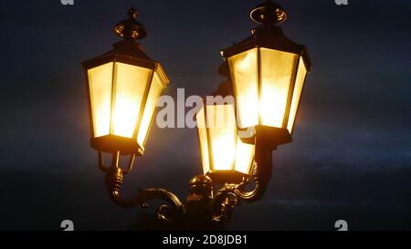 Nahaufnahme von drei altmodischen Laternen in der Nacht mit hell Gelbes Licht und ein unheimlicher dunkler Himmel im Hintergrund Stockfoto