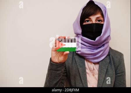 Portrait der jungen muslimischen Frau trägt formelle Kleidung, schützen Gesichtsmaske und Hijab Kopftuch, halten Palästina Flagge Karte vor isoliertem Hintergrund. Koro Stockfoto