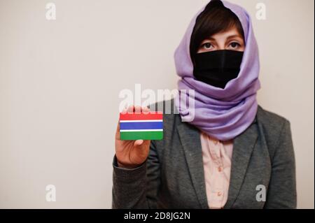 Portrait der jungen muslimischen Frau trägt formelle Kleidung, schützen Gesichtsmaske und Hijab Kopftuch, halten Sie die Gambia Flagge Karte vor isoliertem Hintergrund. Kor Stockfoto
