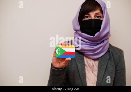 Portrait der jungen muslimischen Frau trägt formelle Kleidung, schützen Gesichtsmaske und Hijab Kopftuch, halten Komoren Flagge Karte vor isoliertem Hintergrund. Corona Stockfoto