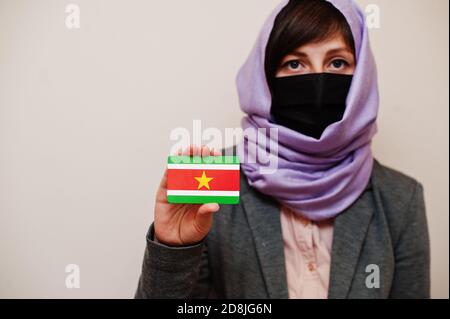 Portrait der jungen muslimischen Frau trägt formelle Kleidung, schützen Gesichtsmaske und Hijab Kopftuch, halten Suriname Flagge Karte vor isoliertem Hintergrund. Coron Stockfoto