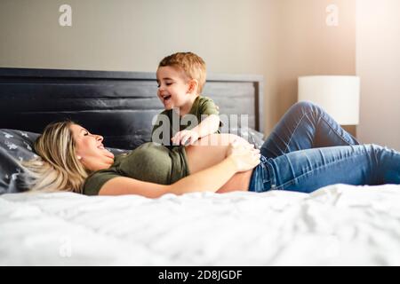 Eine schwangere Mutter und ein Sohn verbringen Zeit zusammen im Schlafzimmer Stockfoto