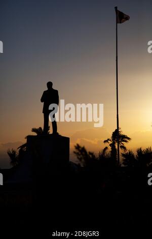 Das Bild zeigt die Silhouette eines Mustafa Kemal Atatürk-Denkmals und einen hohen Fahnenposten, an dem die türkische Flagge bei Sonnenaufgang am vollen Mast fliegt. Es gibt s Stockfoto