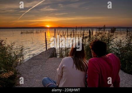 Liebeskonzept. Nicht identifiziertes Hochzeitspaar beobachtet den Sonnenuntergang, der neben dem 'La Albufera' See in Valencia, Spanien, sitzt. Stockfoto