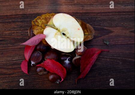 Herbstdekor, rote Blätter, Apfel und Kastanien auf einem Holzbrett Stockfoto