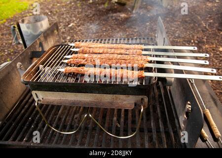 Nahaufnahme des Adana Kebabs, der draußen auf einem klappbaren Holzkohlegrill gegrillt wird. Hackfleisch wird auf Metallspieße befestigt und brutzelt auf Burnin Stockfoto